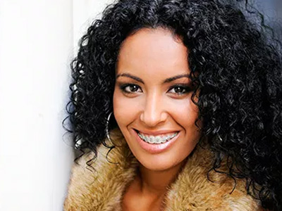 A smiling woman with curly hair, wearing a fur coat and leaning against an open door.