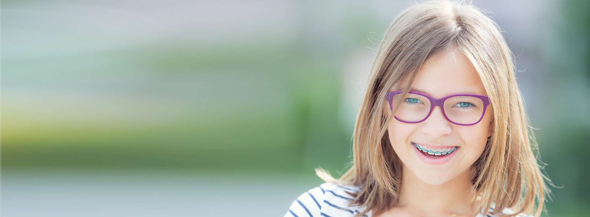 The image shows a young girl with glasses, wearing a white top and smiling at the camera.