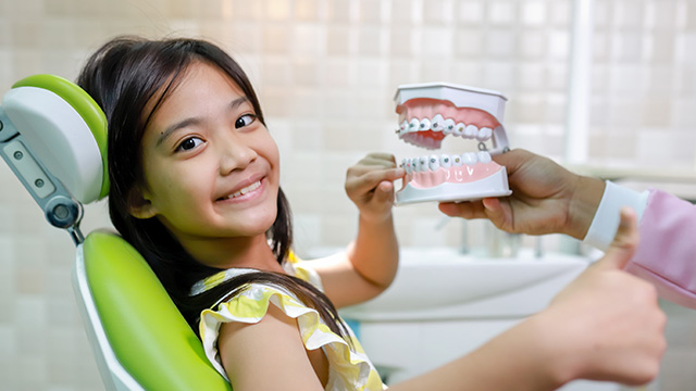 Little girl in dental chair, receiving oral care with smiling face.