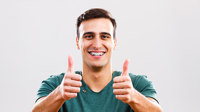 A man giving a thumbs-up gesture with a broad smile, against a white background.