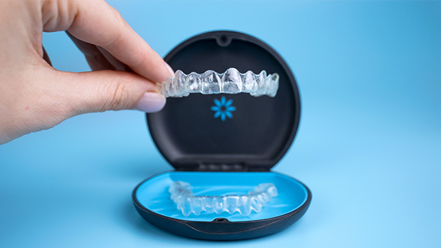 Person holding a clear plastic tray with a blue and white toothbrush, showcasing the bristles.