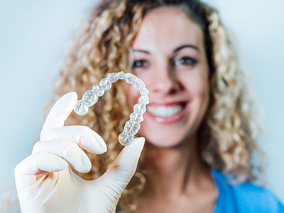 Woman holding transparent dental implant in hand, smiling against white background.